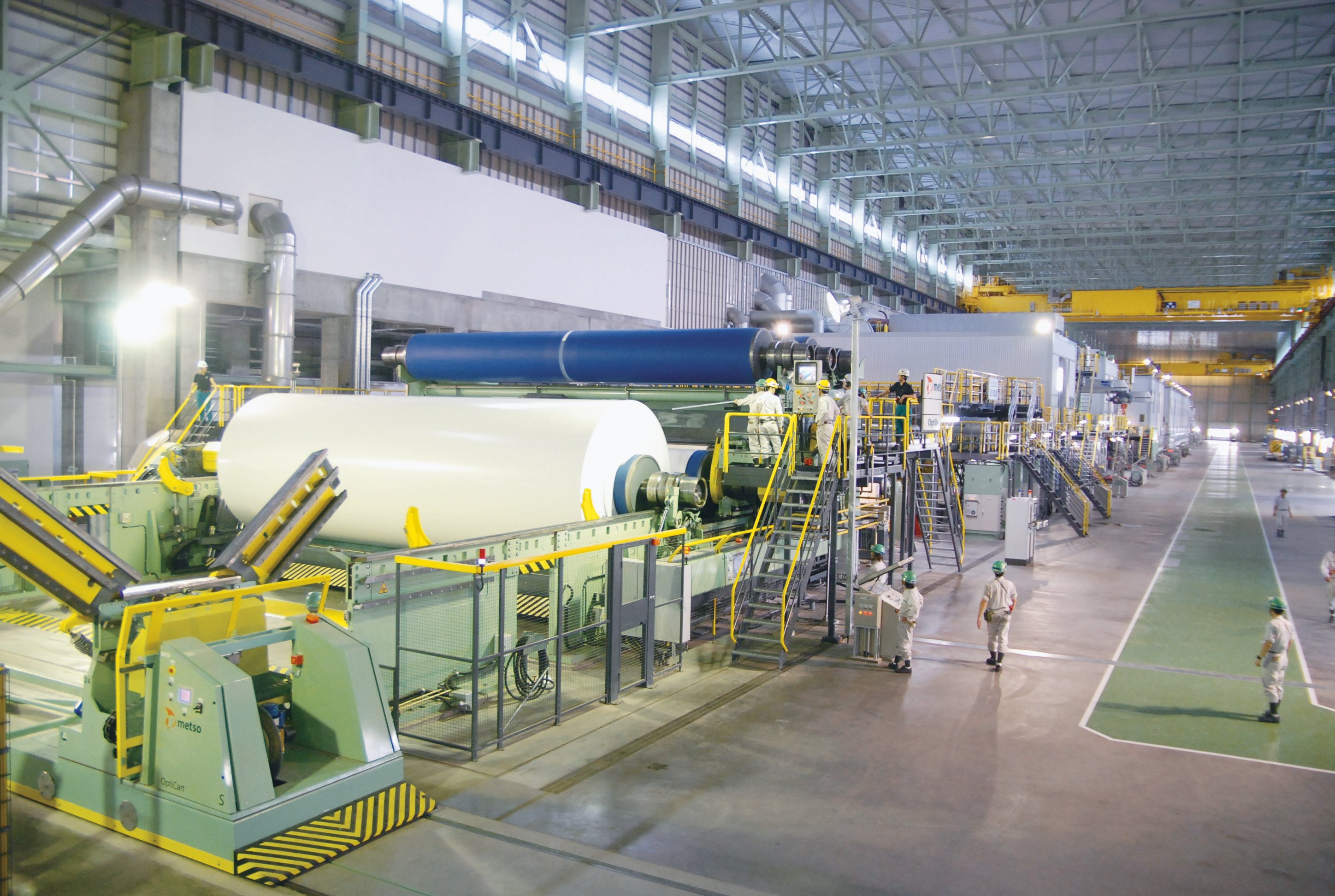 Photo of the No. 9 paper machine operating inside the Niigata Mill, with a large-scale production line and workers on site