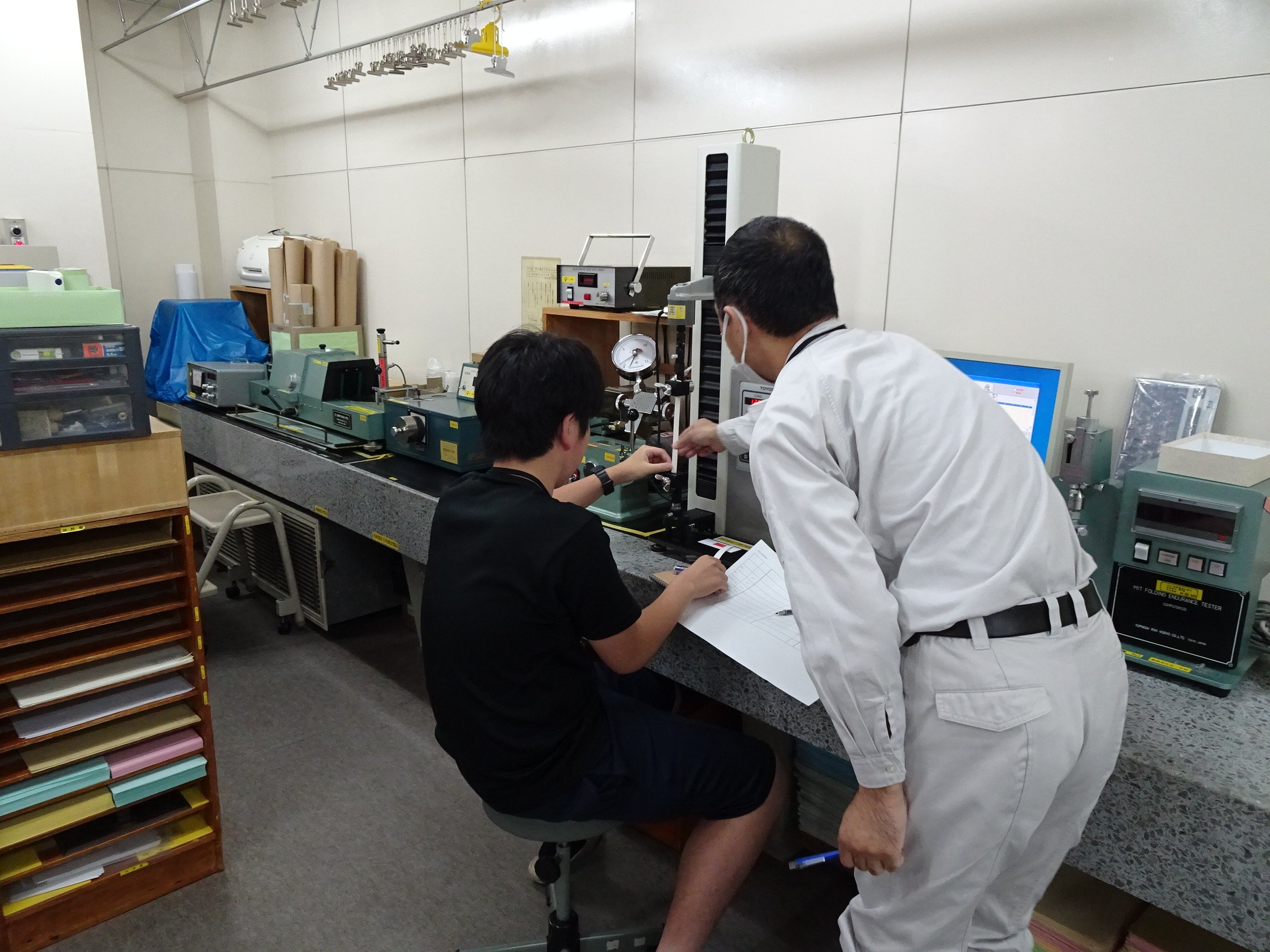 紙の品質試験を実施し、測定機器を操作しながら担当者が試験方法を説明している様子の写真