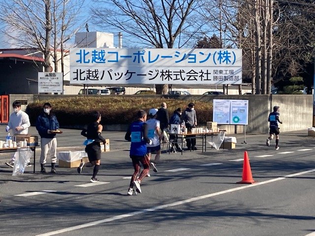 北越コーポレーション関東工場・勝田製造部前のコースを走る参加者と、施設エイドや給水所を設置し、マラソンイベントに協力している様子の写真