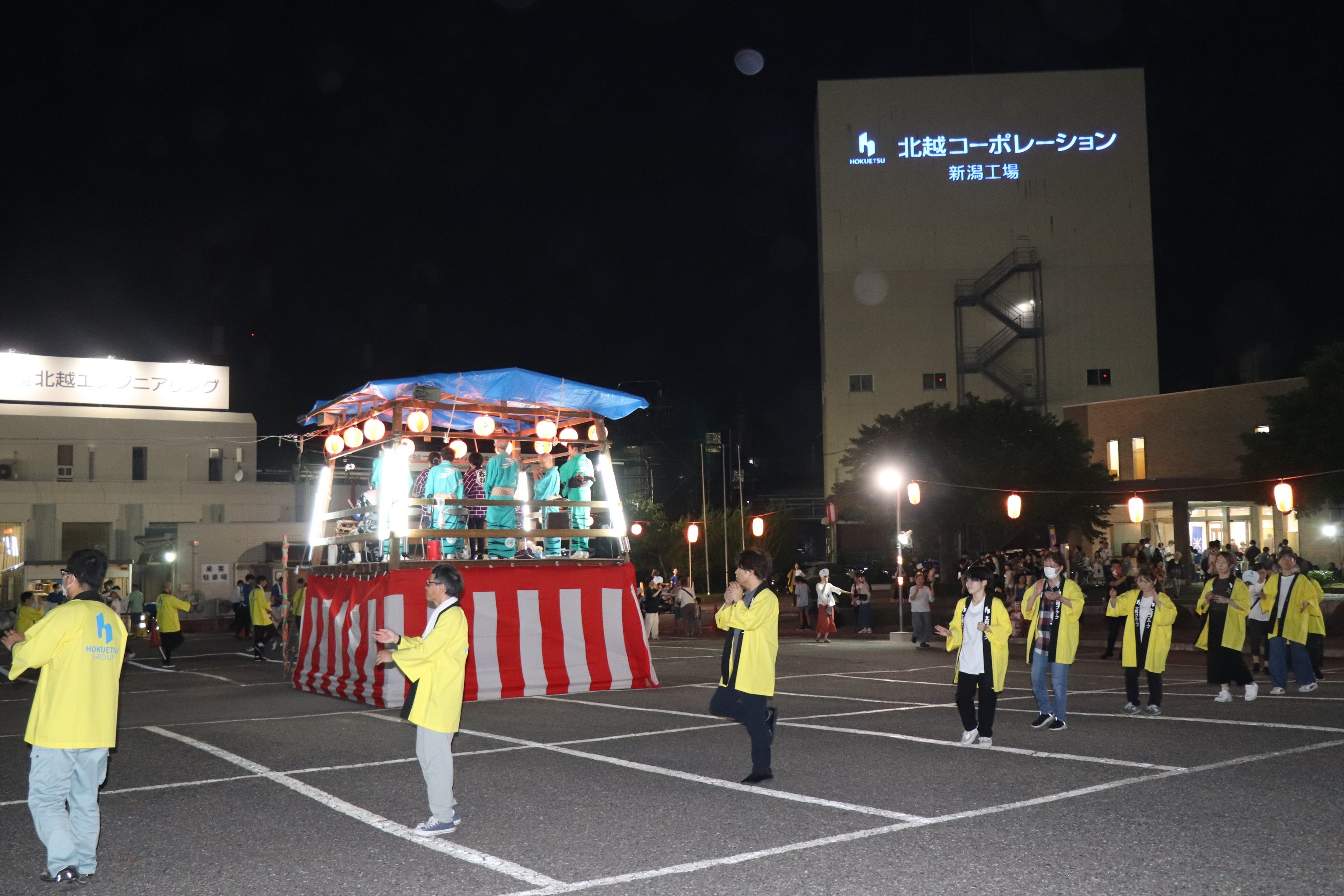 やぐらのまわりで黄色い法被を着た写真が踊る様子。伝統の盆踊り大会を開催した際の写真。